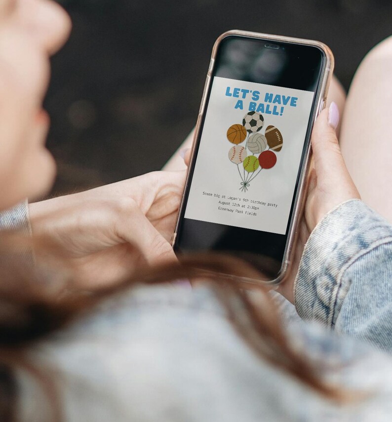 May include: A smartphone displays a sports-themed birthday party invitation. The invitation features a cluster of balloons shaped like sports balls, with the text "LET'S HAVE A BALL!" in blue. Additional text provides party details.