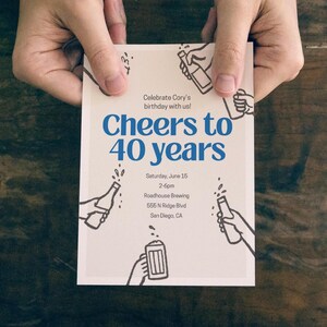 May include: A white invitation card with blue text that reads "Cheers to 40 years." The card includes the text "Celebrate Cory's birthday with us!" and event details. The card is held by two hands, and features illustrations of beer bottles.