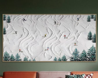 May include: A painting of a snowy mountain scene with skiers and snowboarders. The painting is in a gold frame and is hanging on a green wall above a brown couch. The couch has pillows and a throw blanket.