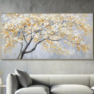 May include: A rectangular canvas painting of a tree with yellow and white leaves. The tree's trunk and branches are grey, set against a light grey background. The painting is framed in gold.