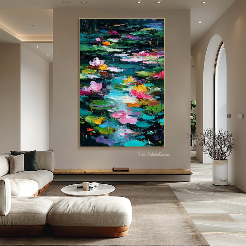 May include: Large, framed abstract painting of a pond with lily pads and flowers. The artwork features vibrant colors, including pink, yellow, and green, with a dark background. The painting is displayed in a modern living room setting.