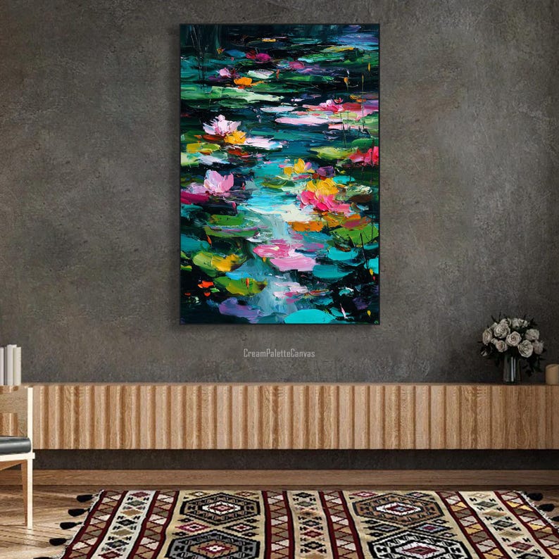 May include: An abstract painting of a pond with lily pads and flowers. The artwork features a vibrant color palette of pink, yellow, and green against a dark background. The painting is displayed on a gray wall above a wooden cabinet.