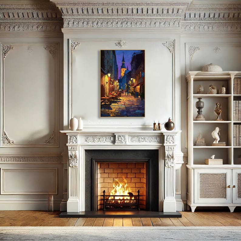 May include: A framed painting depicts a European street scene at dusk. The artwork features a cobblestone street, illuminated by warm streetlights, with buildings on either side. The color palette includes blues, yellows, and oranges, creating a cozy atmosphere.