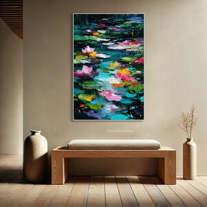 May include: An oil painting of a pond filled with lily pads and vibrant water lilies. The artwork features a palette of pink, yellow, and white flowers, set against a backdrop of green and blue water. The painting is framed in white.