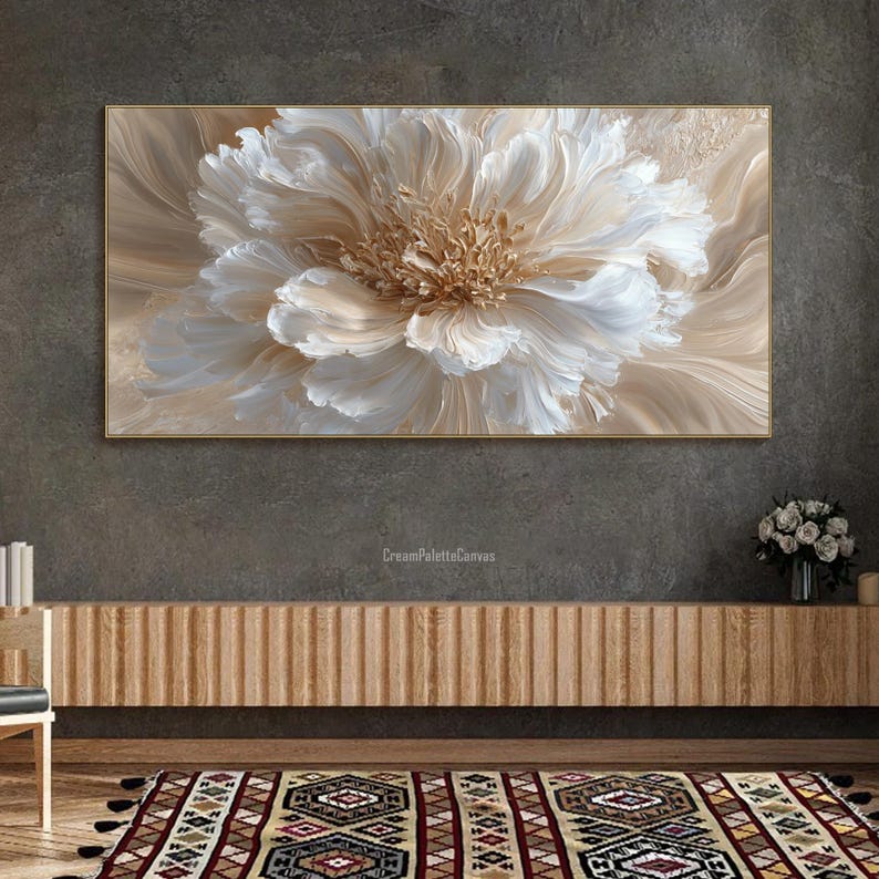 May include: A large, framed floral painting with a textured, three-dimensional effect. The artwork features a central flower in shades of white, cream, and gold, set against a neutral background. The painting is displayed above a wooden cabinet.