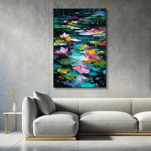 May include: An abstract painting of a pond with lily pads and flowers. The artwork features vibrant colors, including pink, yellow, and teal, with visible brushstrokes. The painting is framed and displayed above a gray sofa.