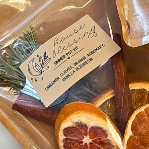 Può includere: Un kit per pentola a fuoco lento con fette d'arancia essiccate, bastoncini di cannella e rosmarino. Il kit include un'etichetta con la scritta "house blessing" e elenca gli ingredienti.