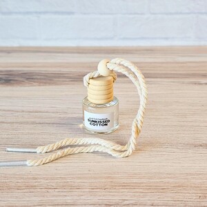 Puede incluir: Una peque&ntilde;a botella de vidrio con una tapa de madera y una etiqueta blanca que dice "Real Fresh Handmade SUNKISSED COTTON" colgando de una cuerda blanca.