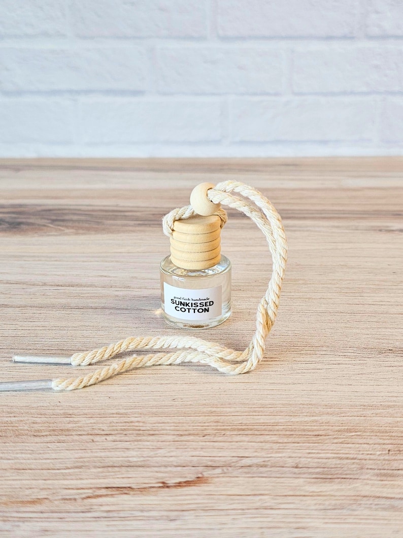 Puede incluir: Una peque&ntilde;a botella de vidrio con una tapa de madera y una etiqueta blanca que dice "Real Fresh Handmade SUNKISSED COTTON" colgando de una cuerda blanca.