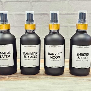 May include: Four black room and linen spray bottles with gold accents and white labels. The labels read "Cashmere Sweater", "Cranberry Sparkle", "Harvest Moon", and "Embers & Fog". Each bottle contains 4 fl oz / 118 ml of product.