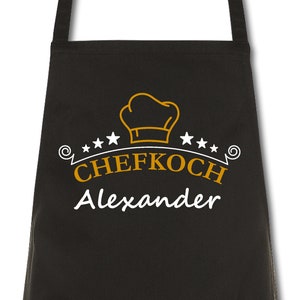 Könnte beinhalten: Schwarze Schürze mit einer weißen Kochmütze und dem Text "CHEFKOCH Alexander" in Gold.