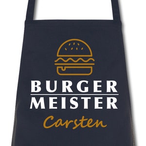 Könnte beinhalten: Marineblaues Kochschürze mit goldener Burger-Umrisszeichnung. Der Text "BURGER MEISTER" ist weiß gedruckt, darunter in Gold "Carsten". Ein Küchenaccessoire für Burger-Liebhaber.