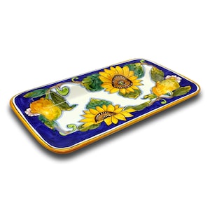 May include: A rectangular ceramic serving tray with a blue background and a yellow rim. The tray is decorated with a white floral pattern featuring sunflowers and lemons.