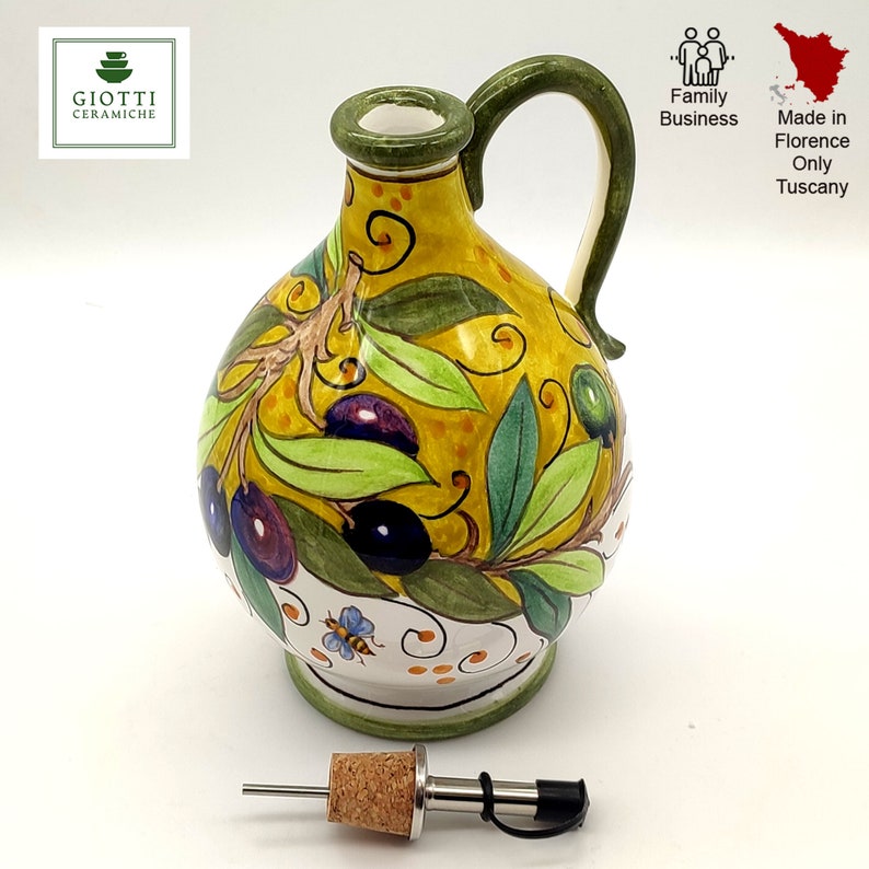 May include: A yellow ceramic olive oil bottle with a green handle and a cork stopper. The bottle is decorated with a hand-painted design of olive branches, leaves, and olives. The bottle is made in Florence, Tuscany, Italy.