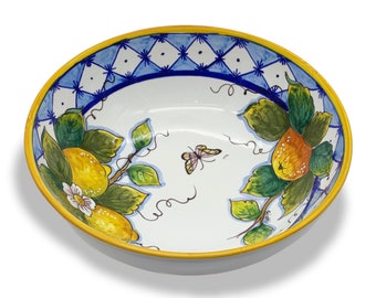 Könnte beinhalten: Eine weiße Keramikschüssel mit gelbem Rand und einem blauen und weißen Rautenmuster am oberen Rand. Die Schüssel ist mit einem handgemalten Design aus Zitronen, Blättern und einem Schmetterling verziert.