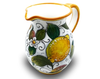 May include: A white ceramic pitcher with a yellow rim and handle. The pitcher is decorated with a lemon motif, featuring yellow lemons, green leaves, and white flowers.