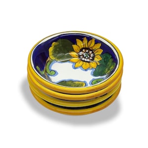 Peut inclure: Ensemble de quatre petits bols en céramique avec un bord jaune et un fond bleu. Les bols sont décorés d'un motif de tournesol peint à la main en jaune, vert et blanc.