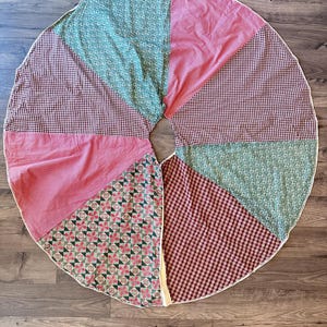 May include: A circular tree skirt featuring a patchwork design of alternating fabric segments. The patterns include solid pink, green floral print, red and white gingham, and a geometric print with red and green shapes on a white background.