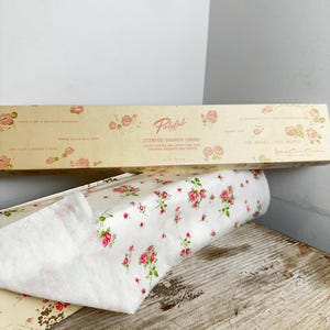 May include: A roll of white scented drawer lining paper featuring a small pink rose and green leaf pattern. The packaging box is cream-coloured with matching floral motifs and text including Polyfab Scented Drawer Lining 108 inches x 12 inches.