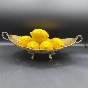 Puede incluir: Un bol de plata con asas ornamentadas y tres patas, lleno de limones amarillos.