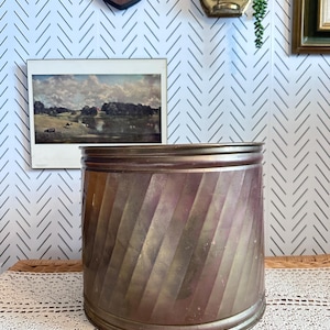 May include: A large, brass planter with a decorative, ribbed design. The planter is slightly curved and has a worn, aged finish.
