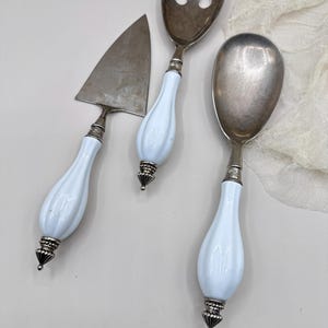 May include: A set of three serving utensils: a pie server, a salad fork, and a serving spoon. Each utensil has a silver head and a light blue, teardrop-shaped handle with silver accents. The set is designed for serving.