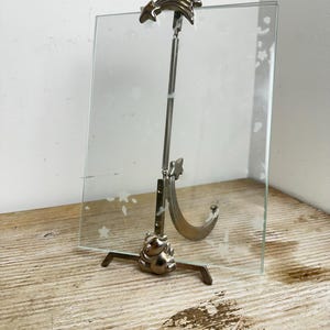 May include: A rectangular glass picture frame featuring a frosted star and moon pattern. The frame is supported by a silver-toned metal stand that includes a spring mechanism, a crescent moon accent, and a shooting star clip at the top.