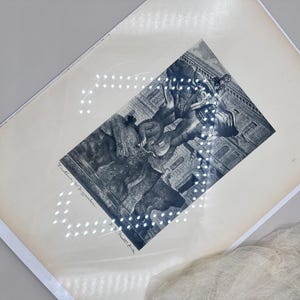 May include: An antique black and white print featuring a detailed illustration of a classical scene with figures and architectural elements. The print is on aged paper, with visible text at the bottom. A soft, white fabric is draped in the corner.