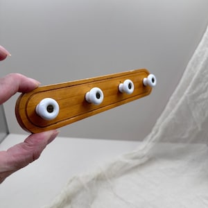 May include: A wooden coat rack with four white ceramic knobs. The rack is a light brown color and has a rounded shape. The knobs are evenly spaced along the rack.