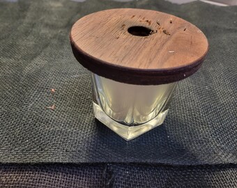May include: A clear glass jar with a wooden lid. The lid has a small hole in the center and is slightly worn.