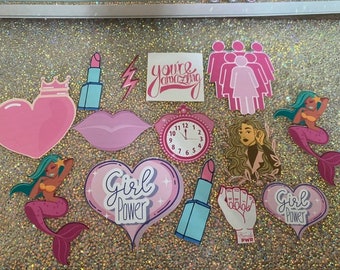 May include: A set of pink and blue stickers with various designs, including hearts, lips, mermaids, a clock, a lightning bolt, a lipstick, and the words "Girl Power" and "You're Amazing".