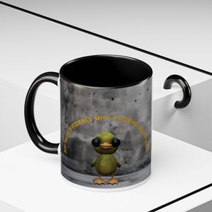 May include: A ceramic mug with a black interior and handle. The exterior features a cartoon duck character with the text "IF NOT FRIEND, WHY FRIEND SHAPED?". The mug has a white base and a gray, textured background.