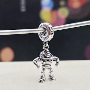 May include: Silver charm featuring a detailed depiction of Buzz Lightyear from the Toy Story franchise. The charm is attached to a silver ring with the inscription "Pandora 59625 ALE TO INFINITI".