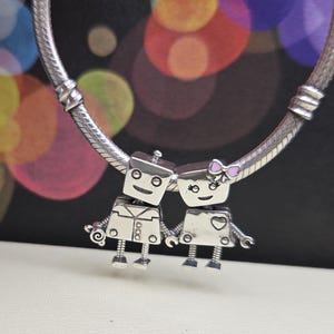 May include: Silver charm bracelet with two robot charms. The robot charms are silver with black details and one has a pink bow.