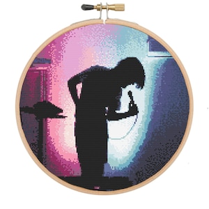 May include: A cross-stitch embroidery hoop with a colorful image of a person singing into a microphone on a stage. The background is a gradient of pink, blue, and purple.