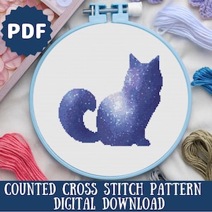 Puede incluir: Patr&oacute;n de punto de cruz contado para un gato galaxia. El patr&oacute;n est&aacute; en un aro azul y el gato es azul oscuro con un dise&ntilde;o de galaxia blanca.