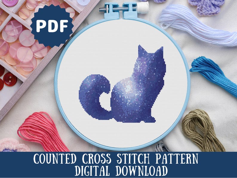 Puede incluir: Patr&oacute;n de punto de cruz contado para un gato galaxia. El patr&oacute;n est&aacute; en un aro azul y el gato es azul oscuro con un dise&ntilde;o de galaxia blanca.