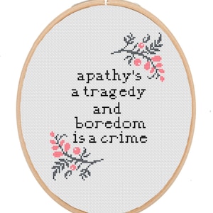May include: A white embroidery hoop with a gray and pink floral design and the text "apathy's a tragedy and boredom is a crime".