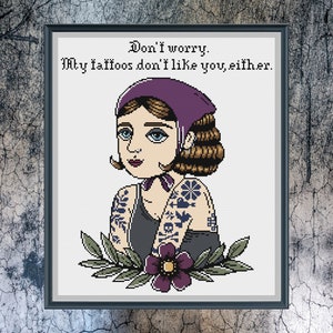 May include: Cross-stitch pattern featuring a woman with purple hair and tattoos, wearing a purple bandana. The text reads "Don't worry. My tattoos don't like you, either."