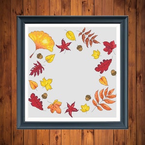May include: A cross-stitch pattern featuring a wreath of autumn leaves in shades of red, orange, and yellow. The leaves are arranged in a circle around a blank space in the center.