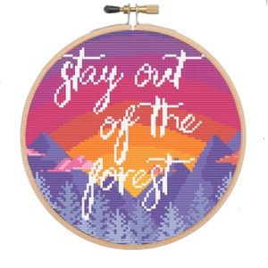 Peut inclure: Broderie au point de croix dans un cercle en bois représentant un coucher de soleil avec des montagnes et des arbres. Le texte "stay out of the forest" est brodé en écriture blanche sur le fond coloré. Une pièce décorative.