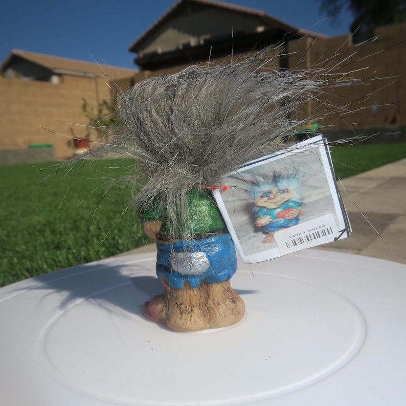 Puede incluir: Una figurita de troll de pelo gris que lleva un atuendo verde y azul. El troll sostiene un coraz&oacute;n rojo en su mano. La figurita est&aacute; de pie sobre una superficie blanca. La figurita tiene una etiqueta adjunta que dice "Edici&oacute;n limitada".