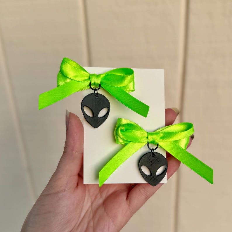 May include: A pair of earrings with neon green bows and black alien head charms.