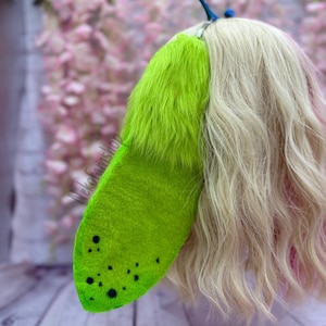 May include: A bright green faux fur tail with black spots, attached to a wig with blonde and pink hair.
