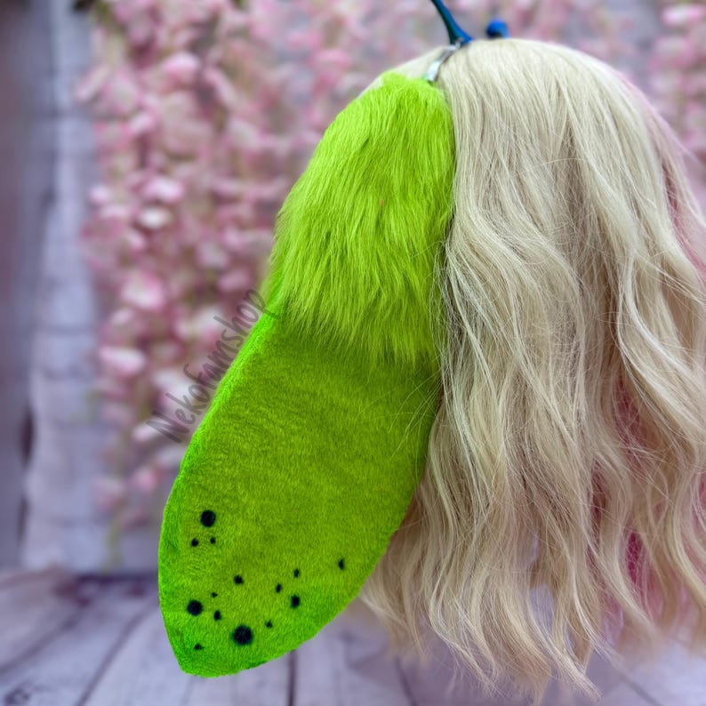May include: A bright green faux fur tail with black spots, attached to a wig with blonde and pink hair.