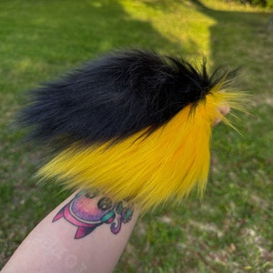 May include: A black and yellow faux fur tail. The tail is fluffy and has a split colour design, with black fur on the top half and yellow fur on the bottom half.
