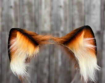 Könnte beinhalten: Ein Stirnband mit Fuchs-Ohren aus braunem und weißem Fell. Das Stirnband ist aus klarem Kunststoff.