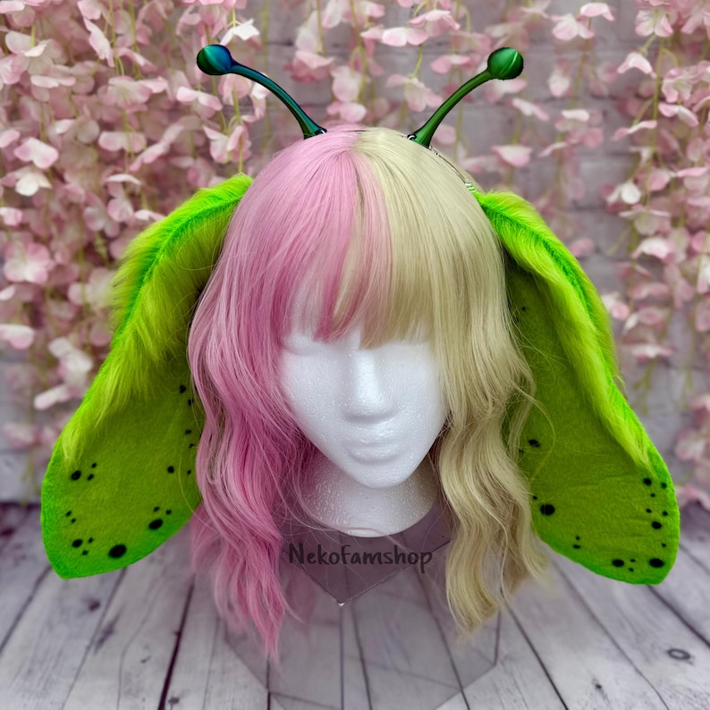 May include: Green and black fuzzy ear headband with iridescent green antennae. The headband is worn by a mannequin with pink and blonde hair. The text "Nekofamshop" is visible on the mannequin's chest.