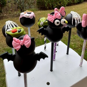 Puede incluir: Un conjunto de seis cake pops con tem&aacute;tica de Halloween decorados con murci&eacute;lagos, esqueletos y caramelos. Los cake pops est&aacute;n en palos y dispuestos en una caja blanca.