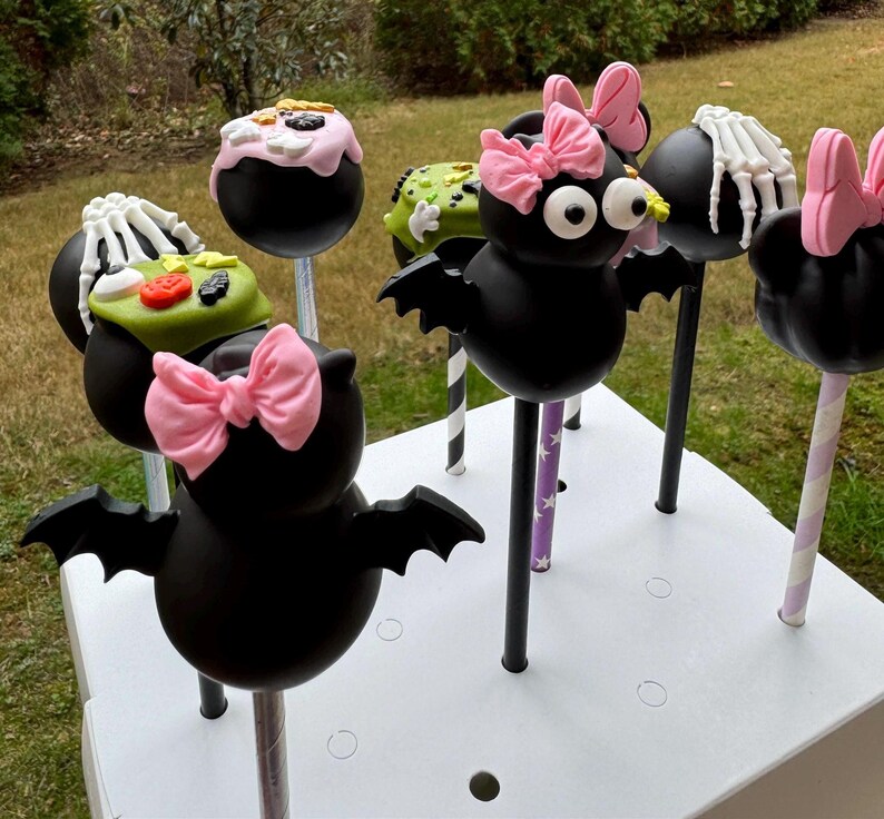 Puede incluir: Un conjunto de seis cake pops con tem&aacute;tica de Halloween decorados con murci&eacute;lagos, esqueletos y caramelos. Los cake pops est&aacute;n en palos y dispuestos en una caja blanca.